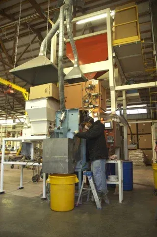 Worker operating a machine in an industrial warehouse with metal ducting and bins