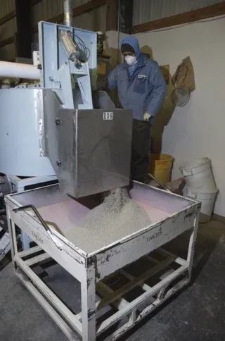 Worker in blue protective gear operating a machine over a bin of grain in an industrial room
