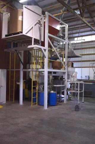 Industrial metal platform with ladder, blue barrel, and machinery inside a warehouse.