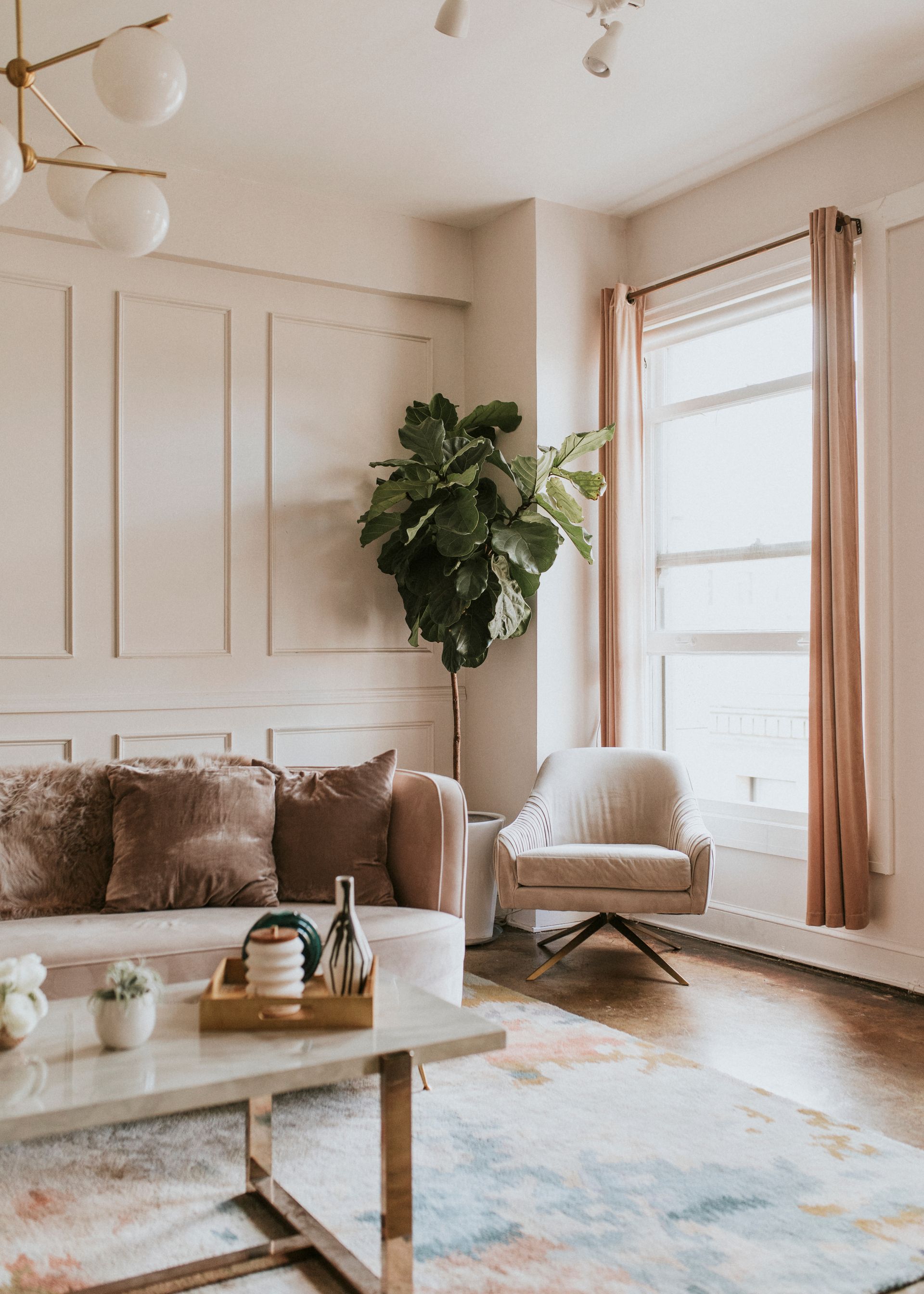 Cozy living room with beige sofa, white chair, coffee table, large plant, and soft natural light.