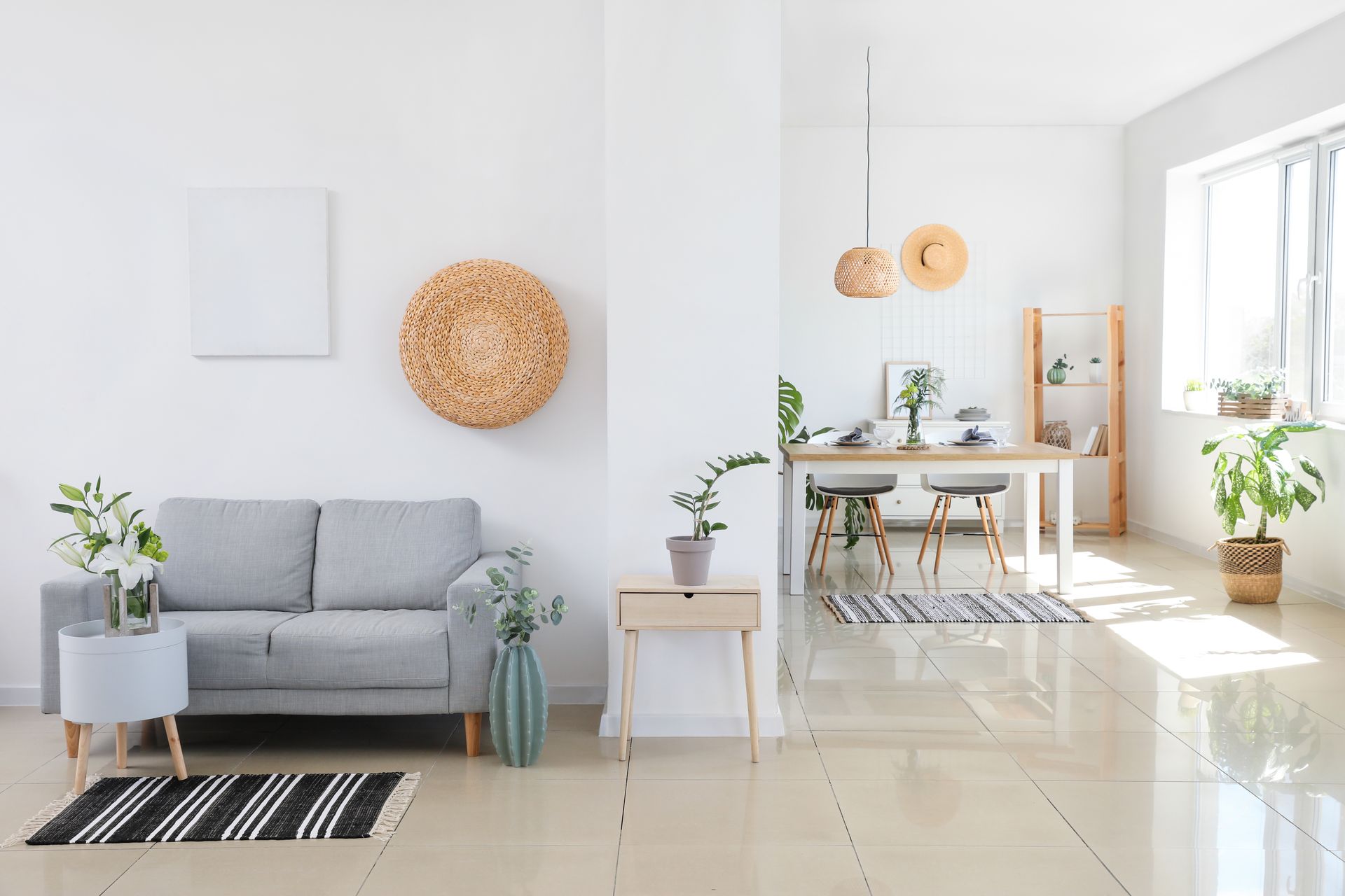 Bright minimalist living room with gray sofa, plants, and sunlit dining area