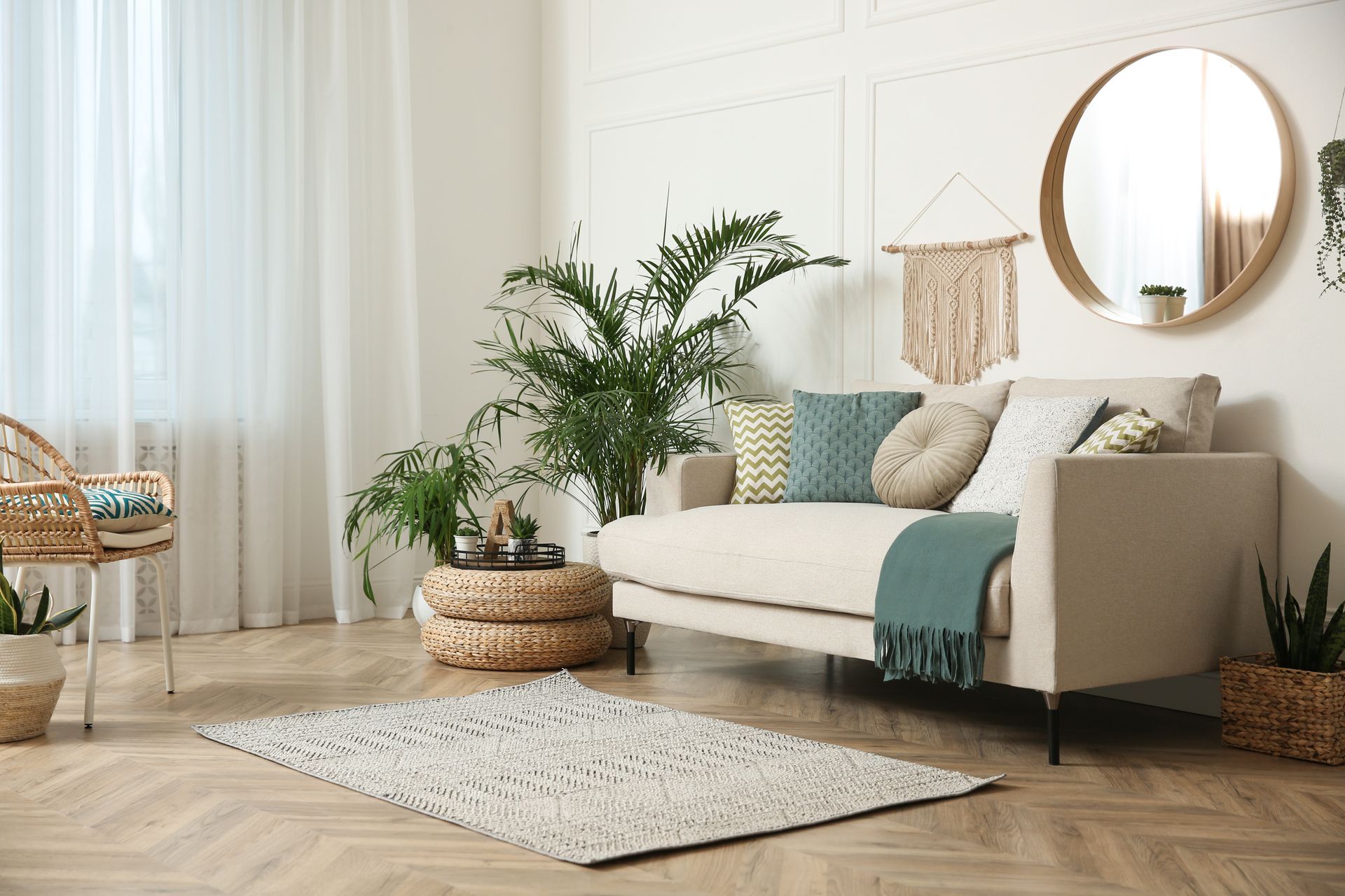 Bright boho living room with cream sofa, teal accents, plants, round mirror, and woven decor