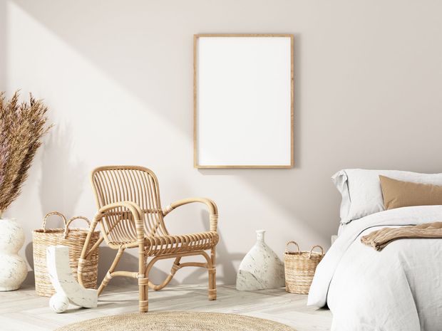 Minimalist bedroom with wicker chair, neutral decor, and a blank framed print on the wall