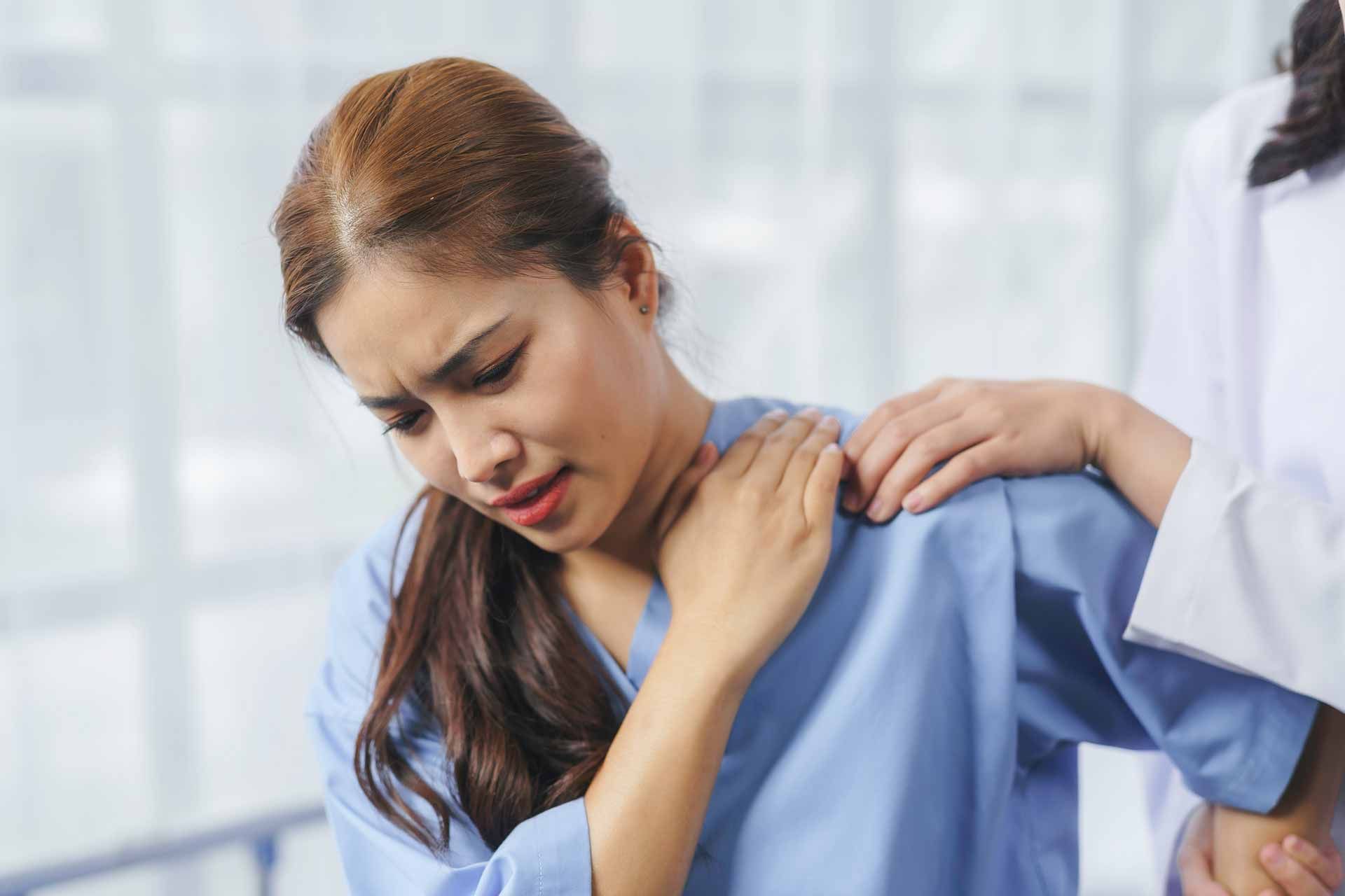 Woman in blue medical scrubs holding her shoulder with a pained expression while being assisted