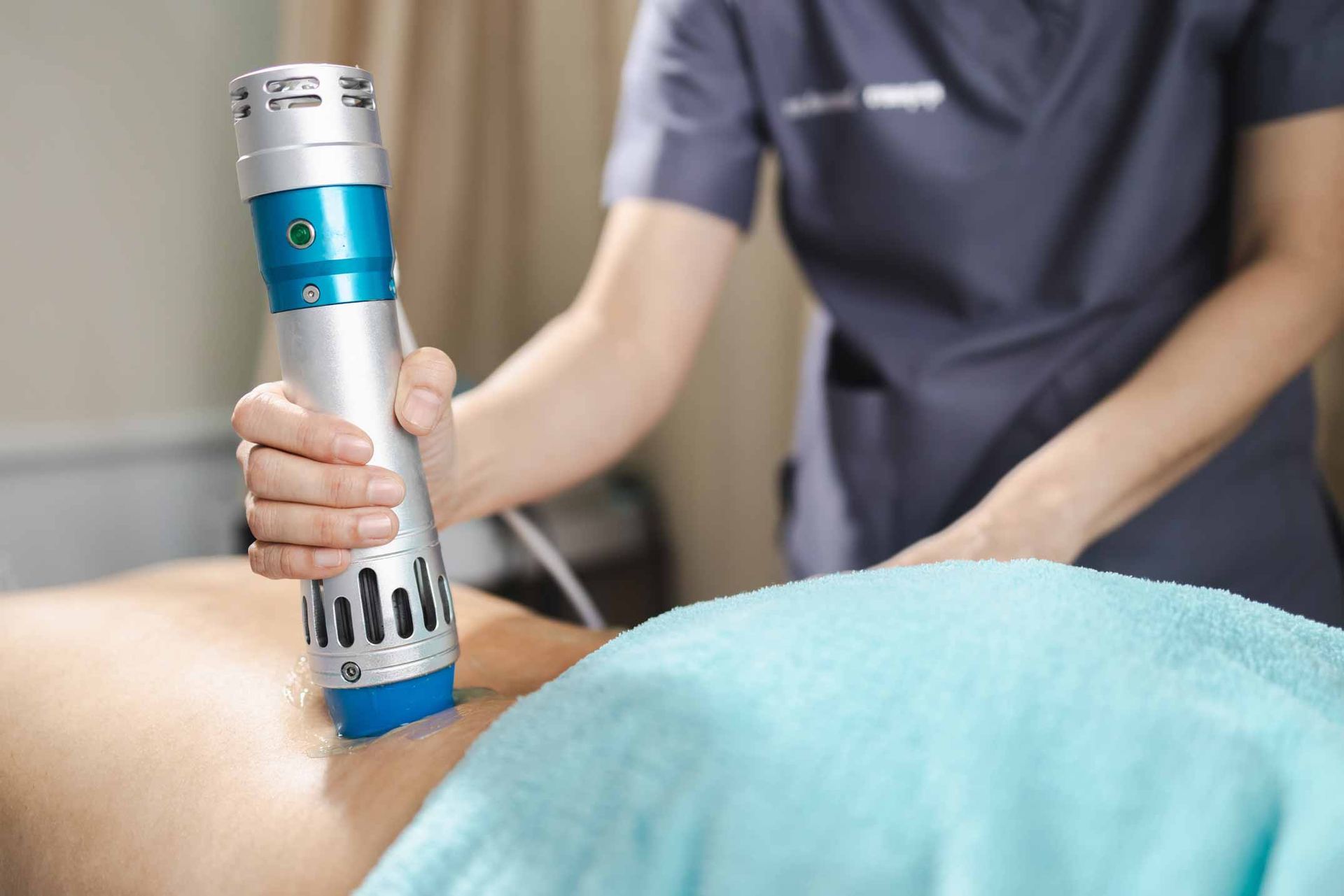 Therapist using a handheld massage device on a patient’s bare back.