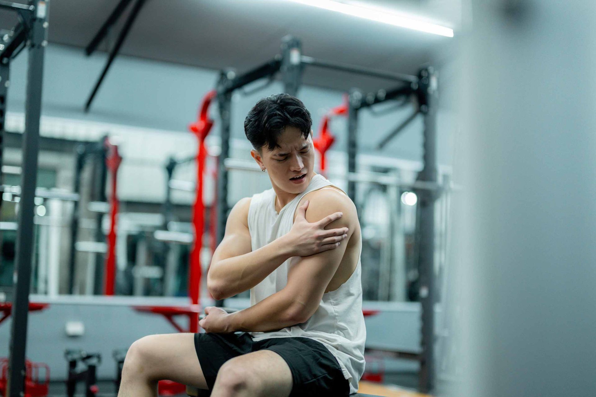 Person in a gym rubbing their shoulder while seated on a bench.