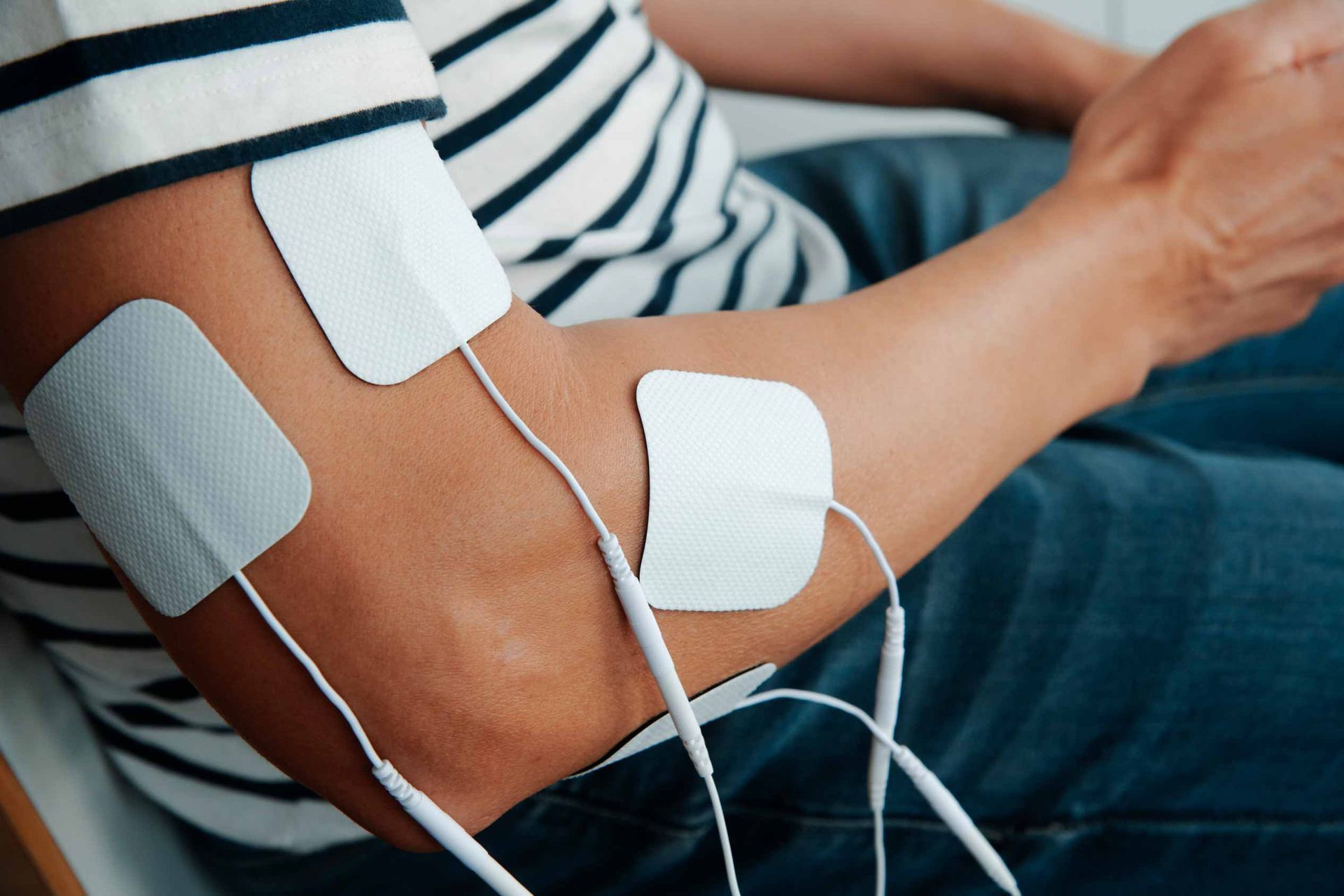 Person’s arm with white electrotherapy pads and wires attached, resting on a sofa