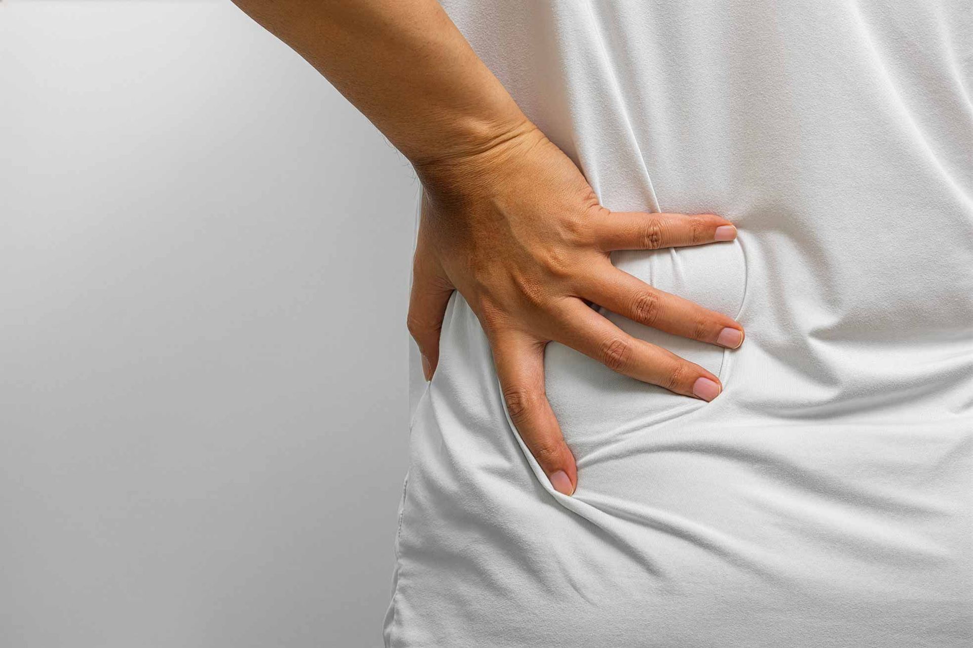 Hand pressing lower back in white shirt, suggesting back pain