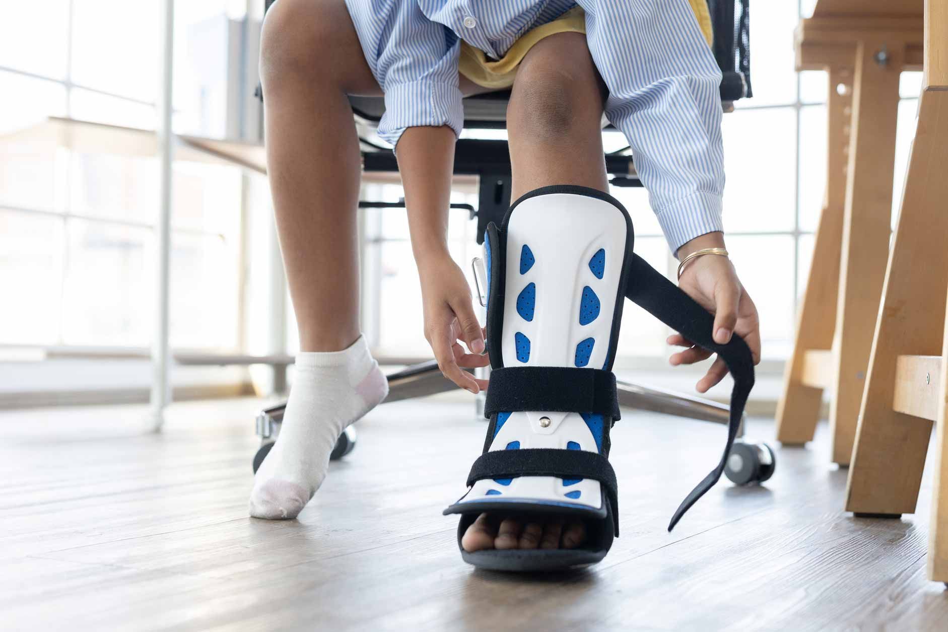 Person fastening a white-and-blue medical walking boot while seated indoors