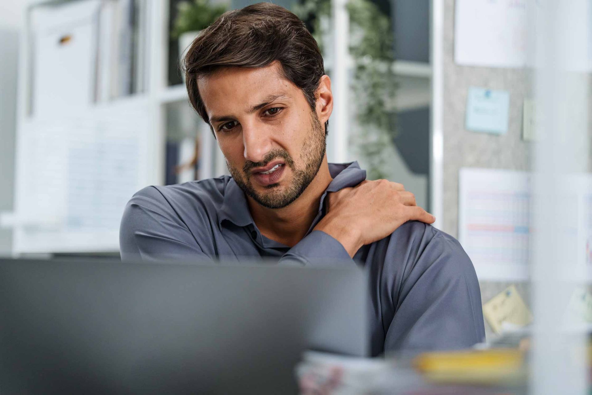 Person rubbing shoulder while looking at a laptop in an office setting