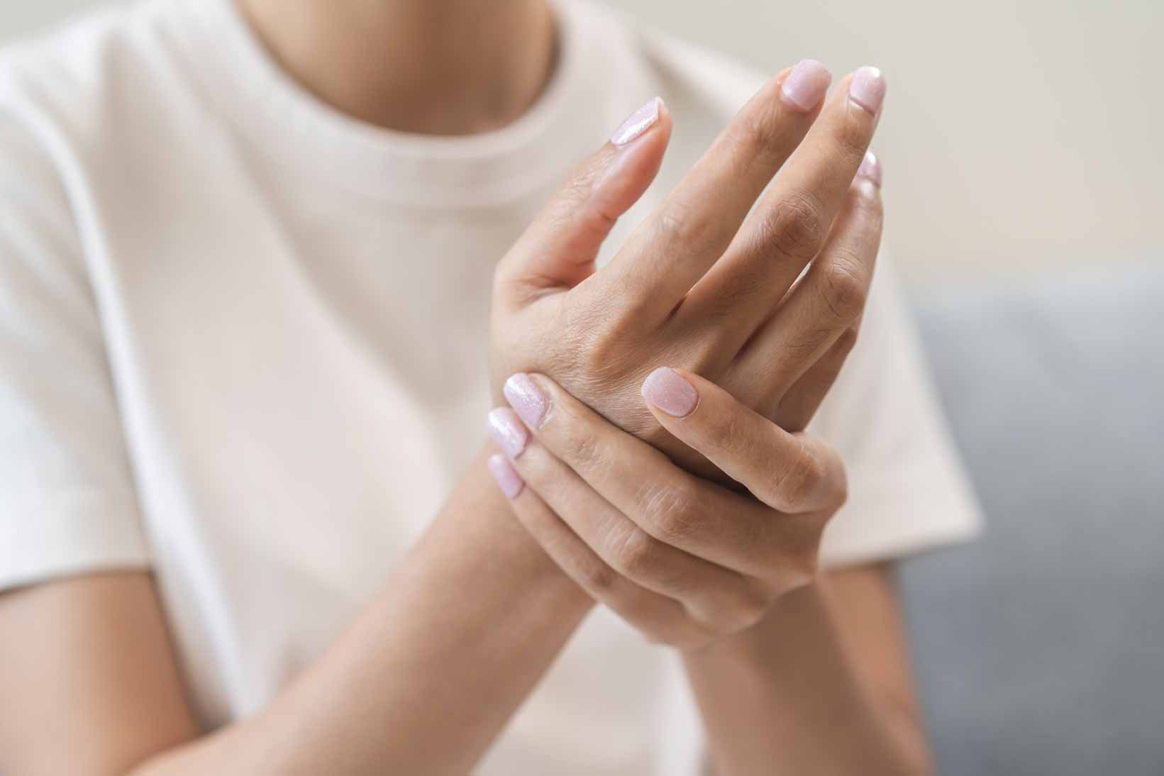 Person holding their wrist with one hand, suggesting pain or discomfort, in a soft indoor setting