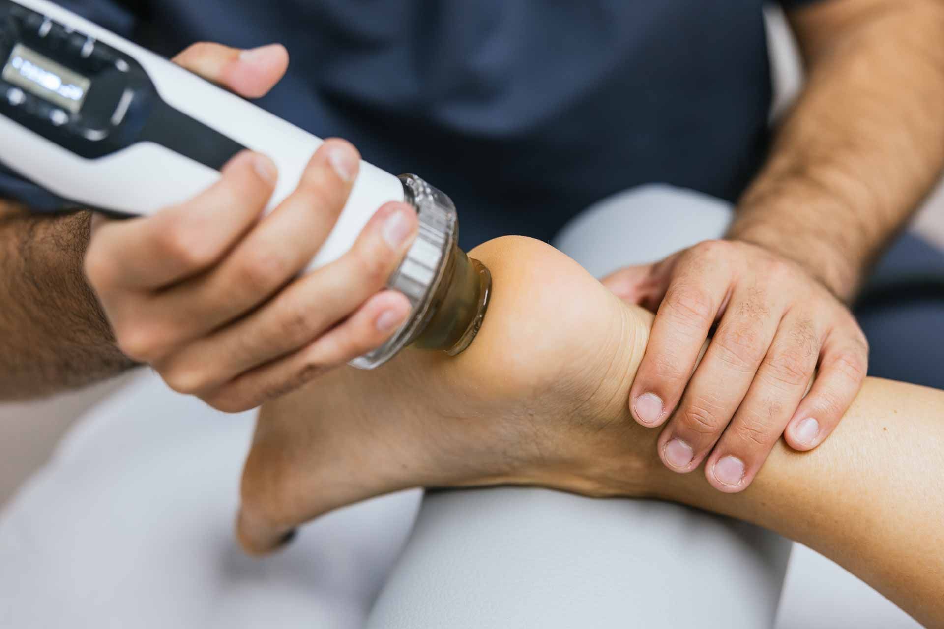 Physiotherapist using a handheld device on a patient’s ankle during treatment