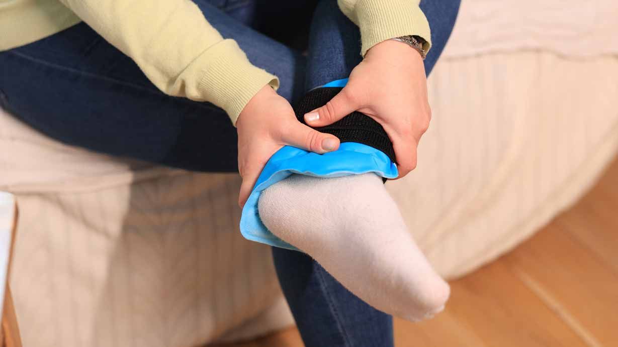 Person putting a blue sock on a seated child’s foot near a beige couch