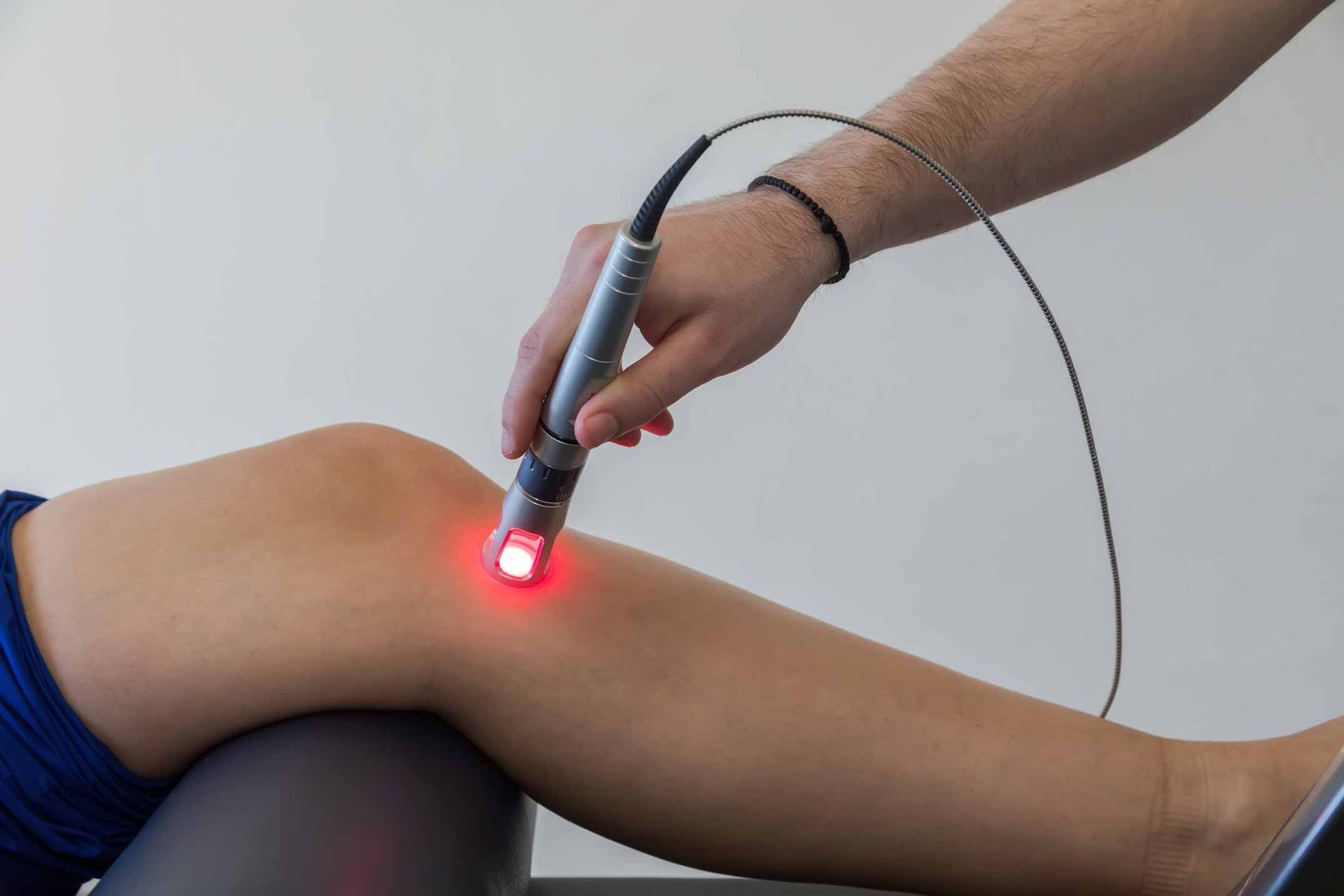 Therapist using a handheld red laser device on a person’s bent knee during treatment