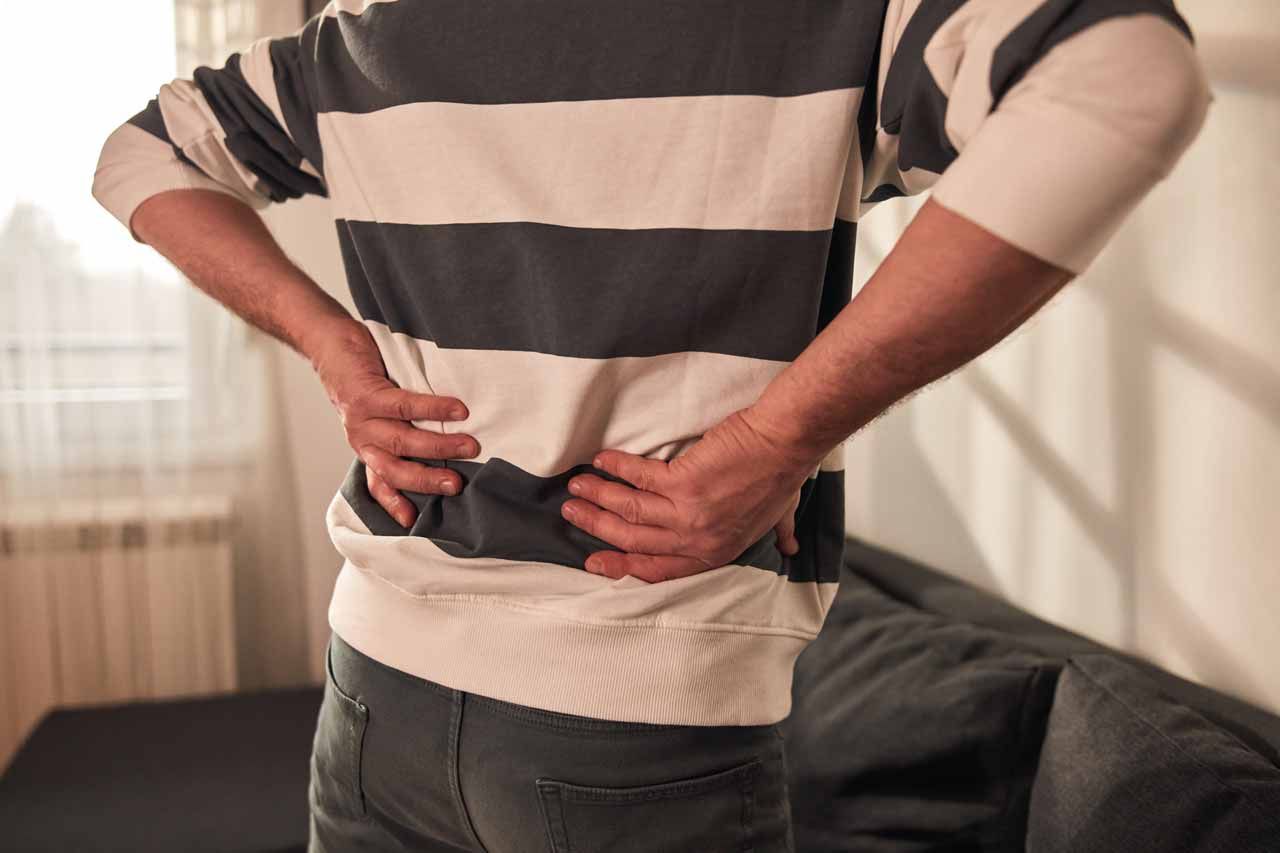 Person holding lower back while standing in a living room, suggesting back pain.