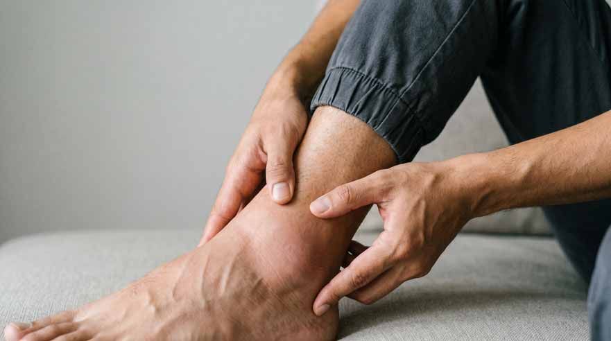 Hands massaging an ankle on a gray couch