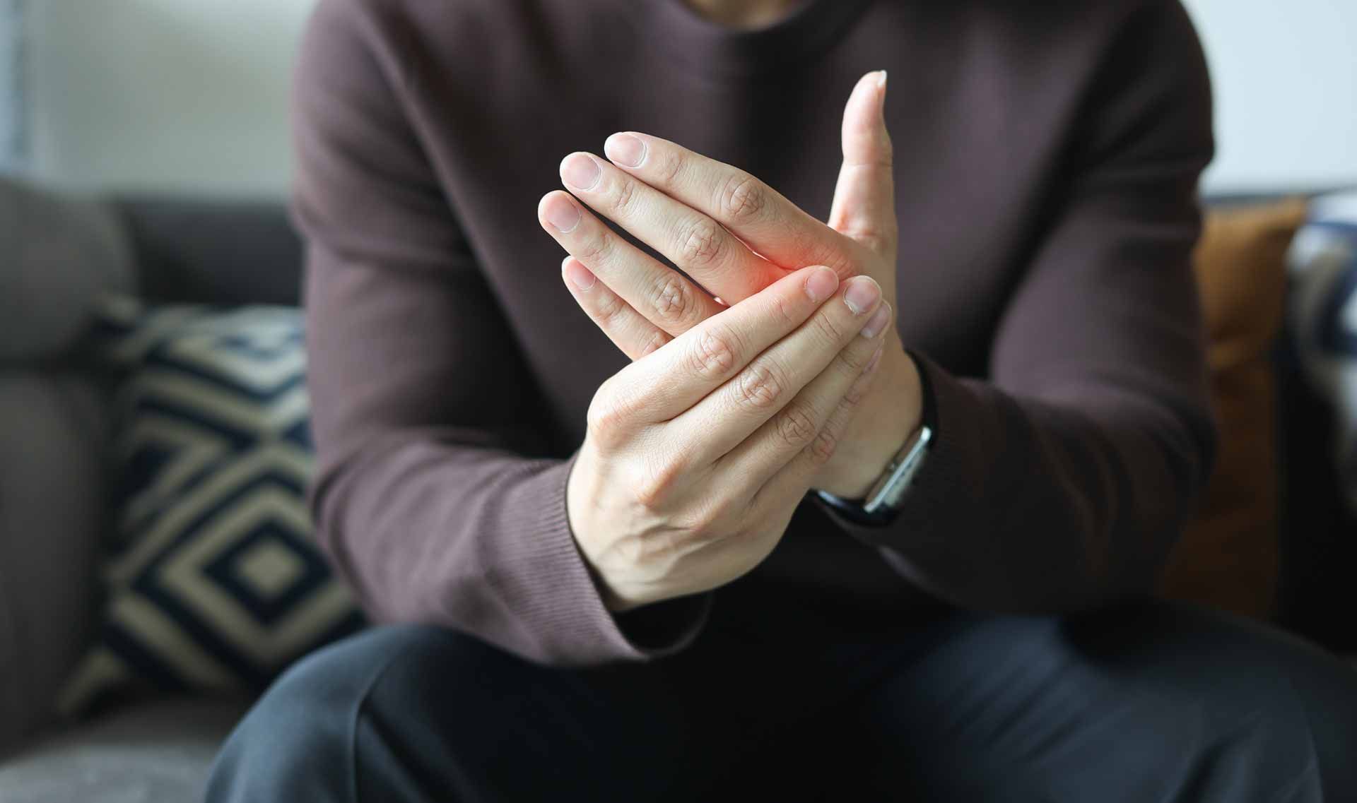 Close-up of hands clasping together on a couch, wearing a dark long-sleeve shirt.