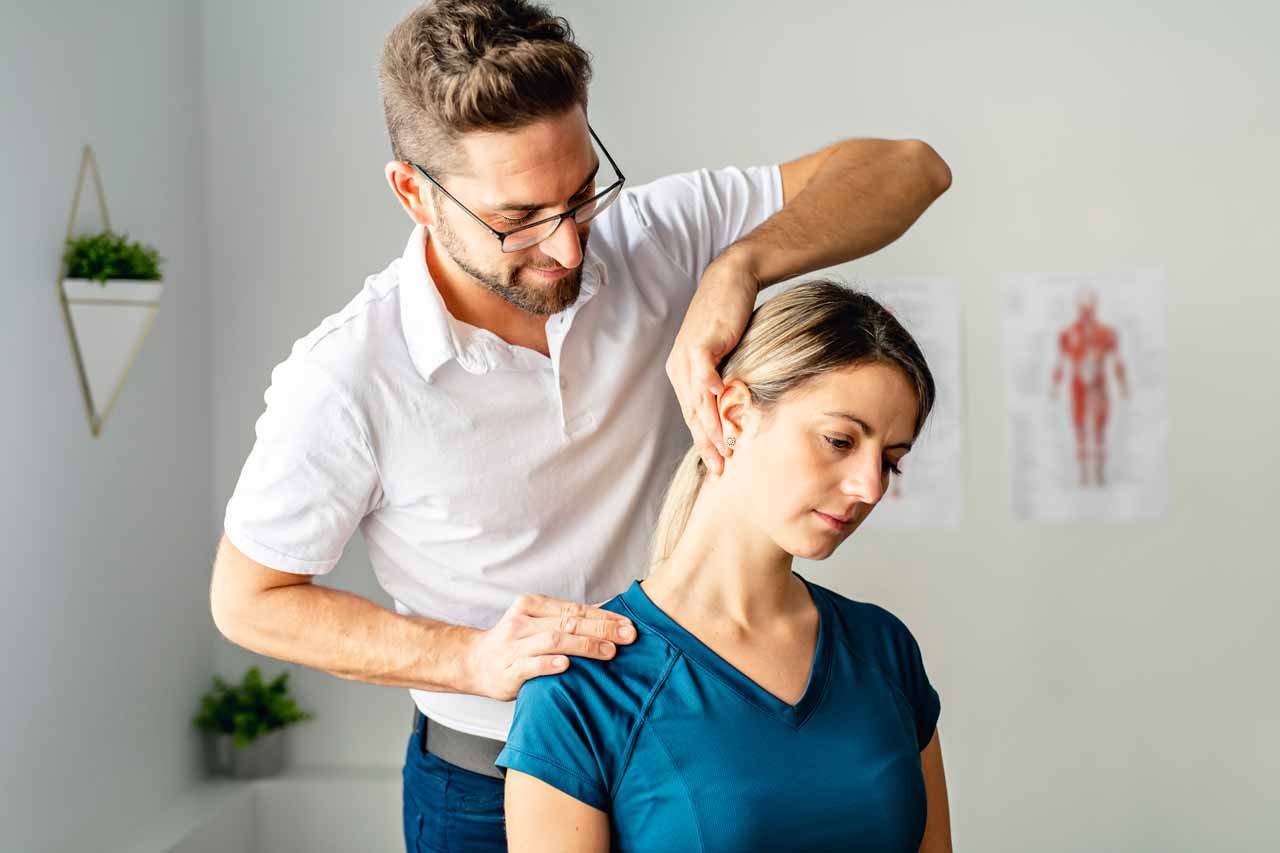 Physical therapist adjusting a woman’s shoulder during a clinic session, with a posture diagram in the background