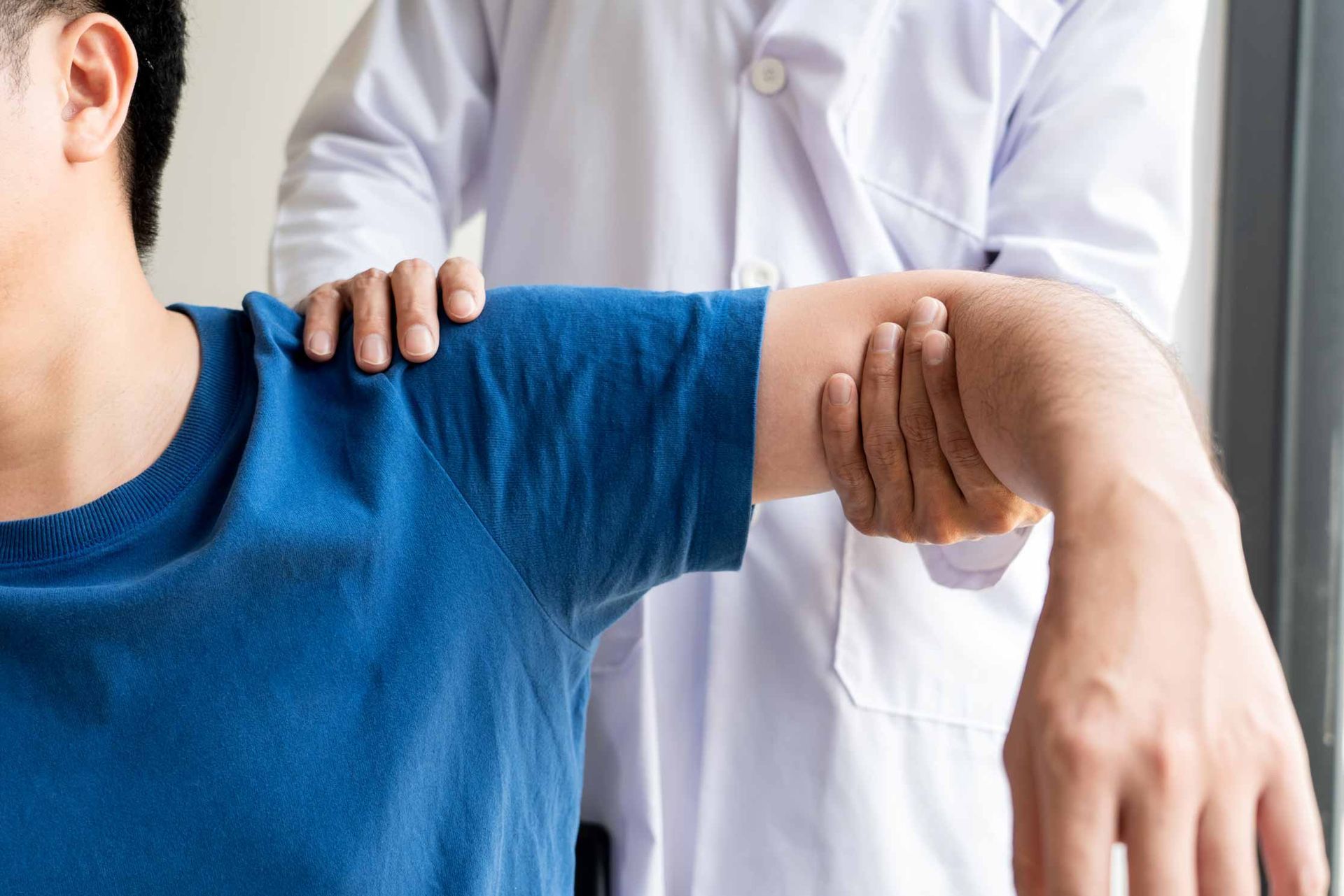 Doctor examining a patient’s arm in a clinic, with the patient wearing a blue shirt