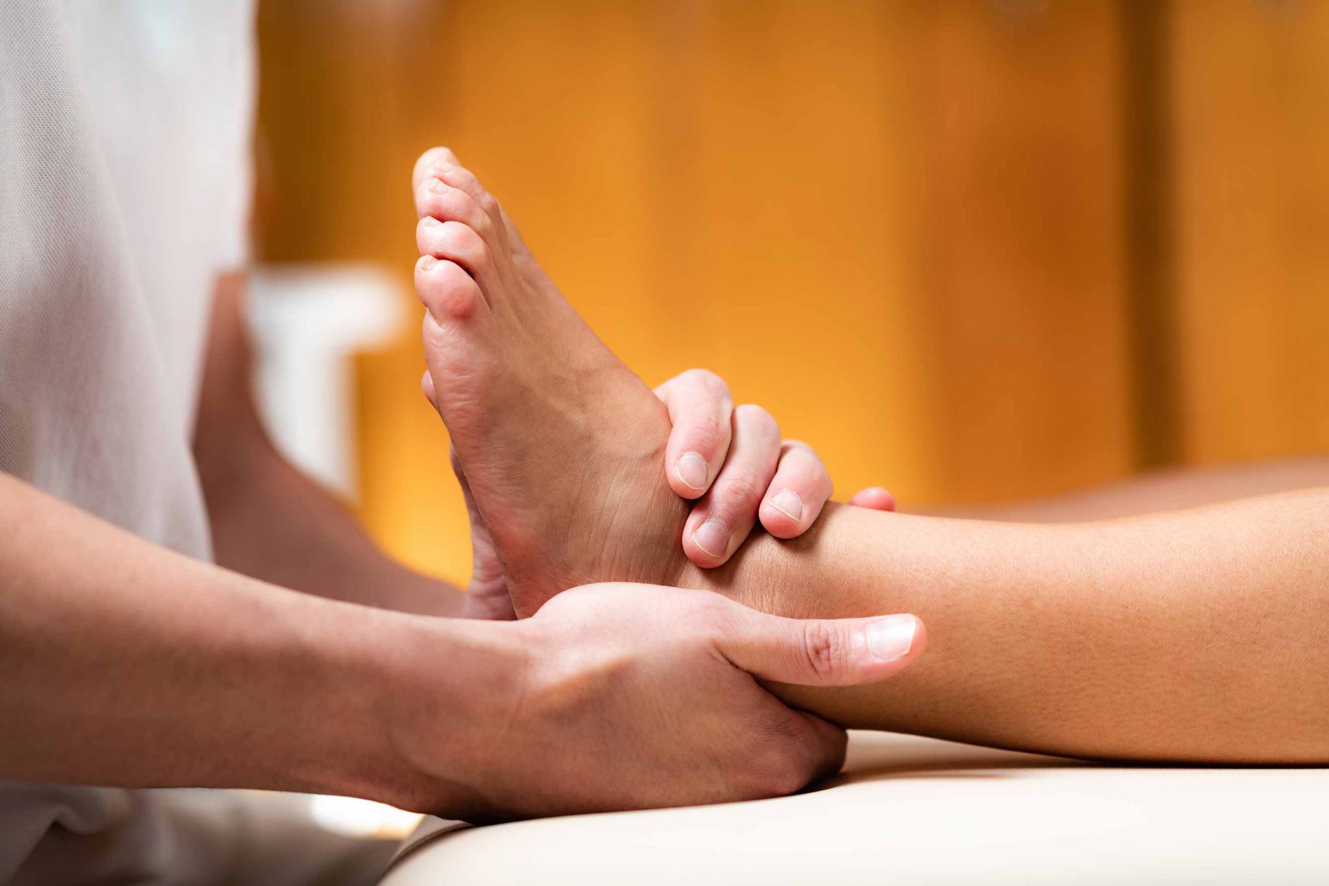 Hands massaging a bare foot on a wooden table, with a warm blurred background