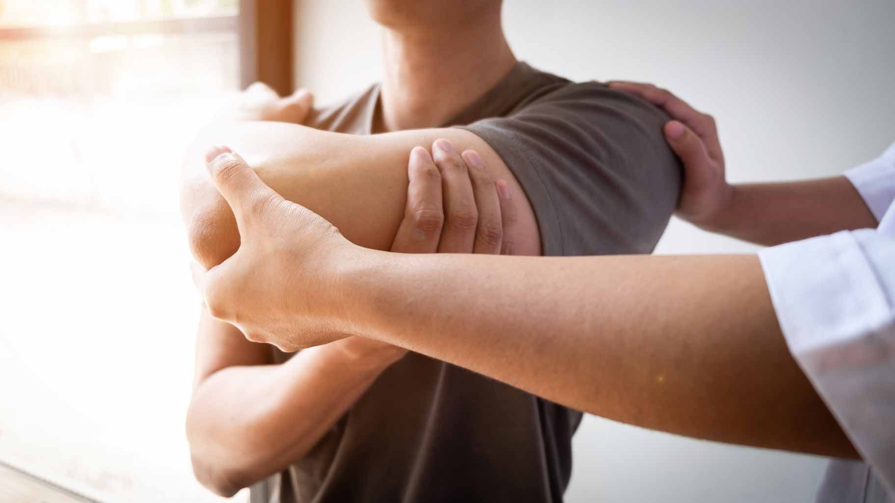 Two people stretching an arm in a bright indoor setting