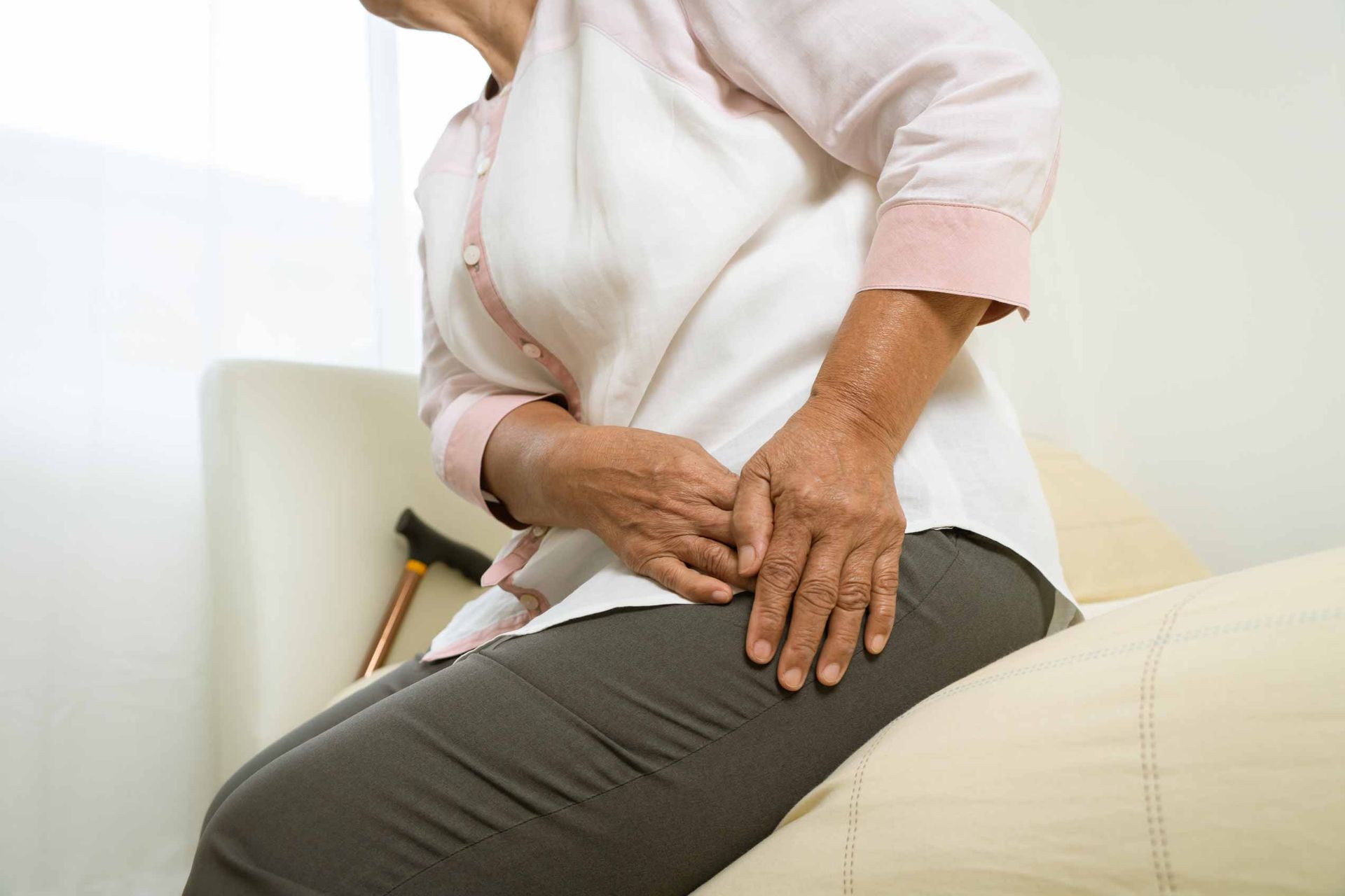 Person clutching a painful lower back while sitting on a couch