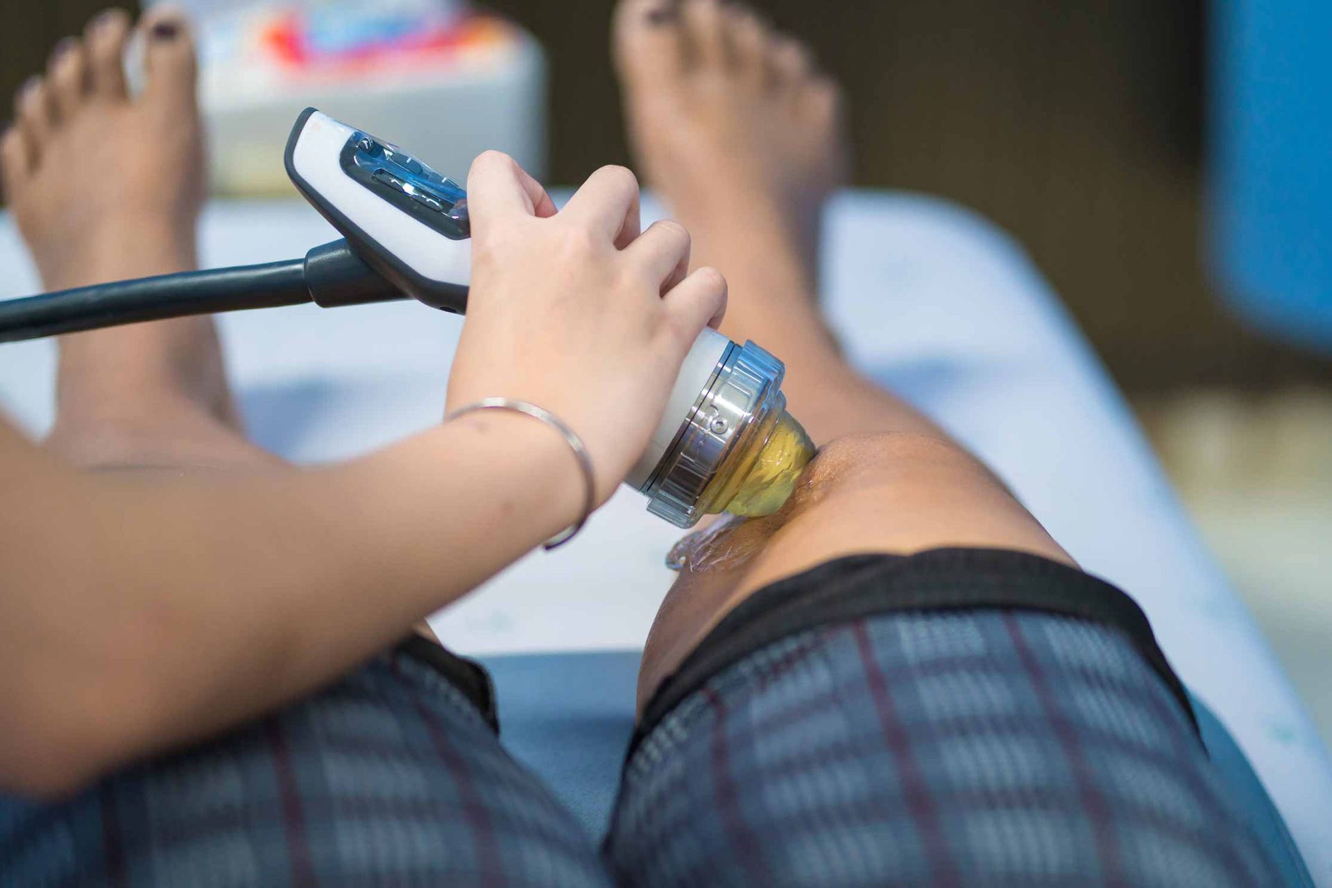 Close-up of a person holding a handheld device against a patient’s leg on a medical exam table