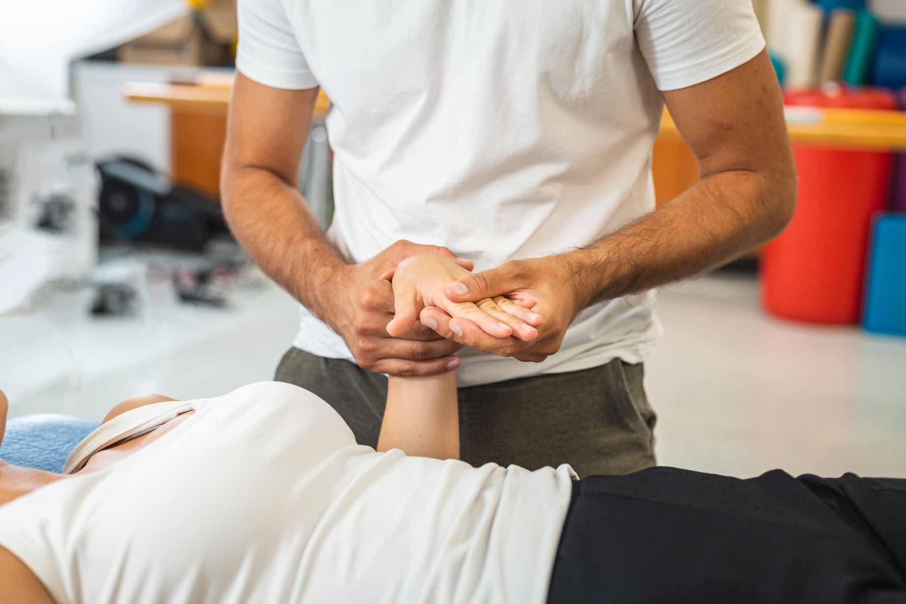 Therapist holding a patient’s arm during treatment on a table in a bright clinic