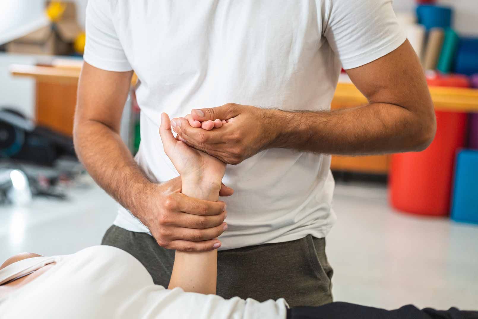 Person holding another person's wrist during a physical therapy or first aid assessment indoors