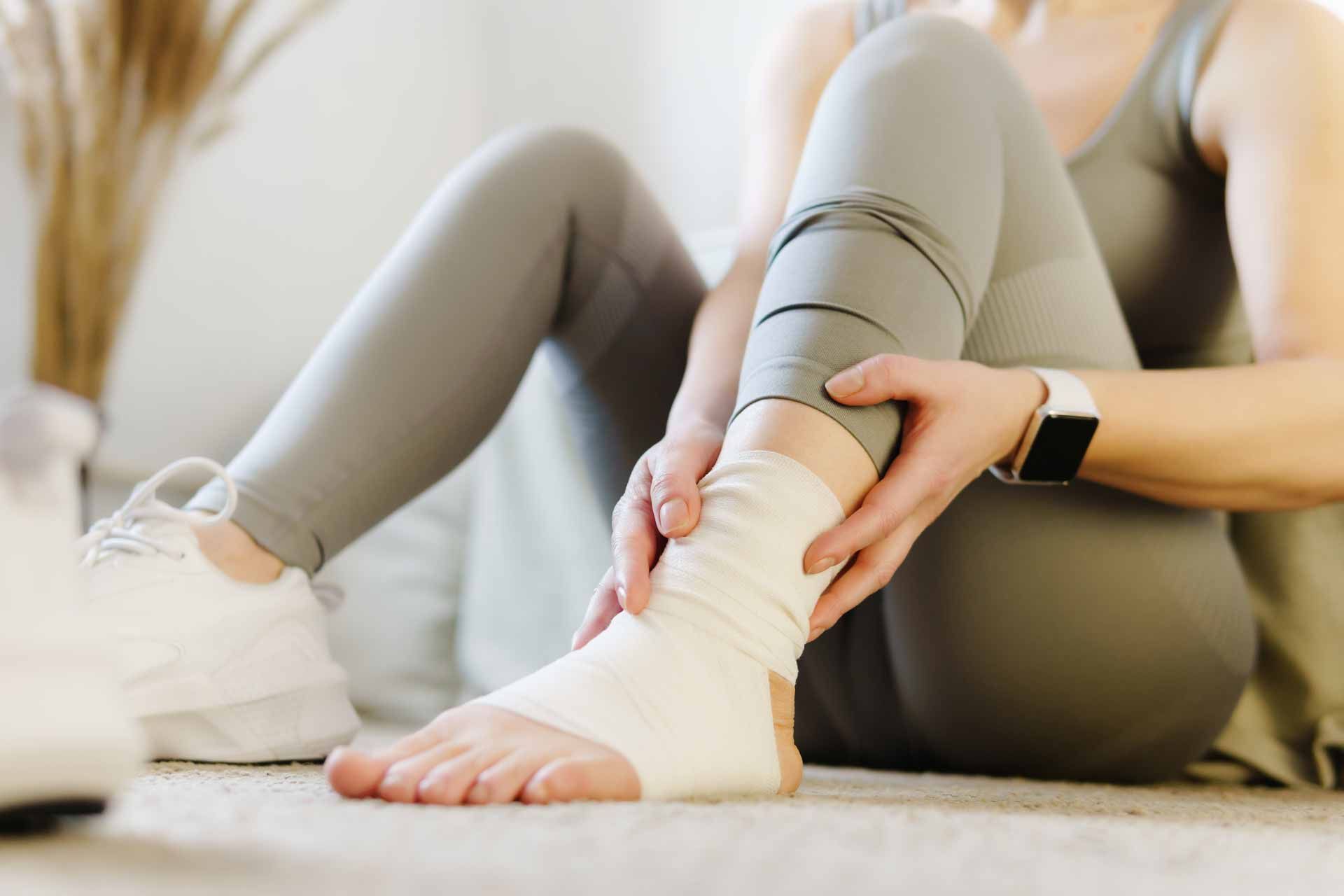Person wrapping a bandage around an ankle while seated on the floor