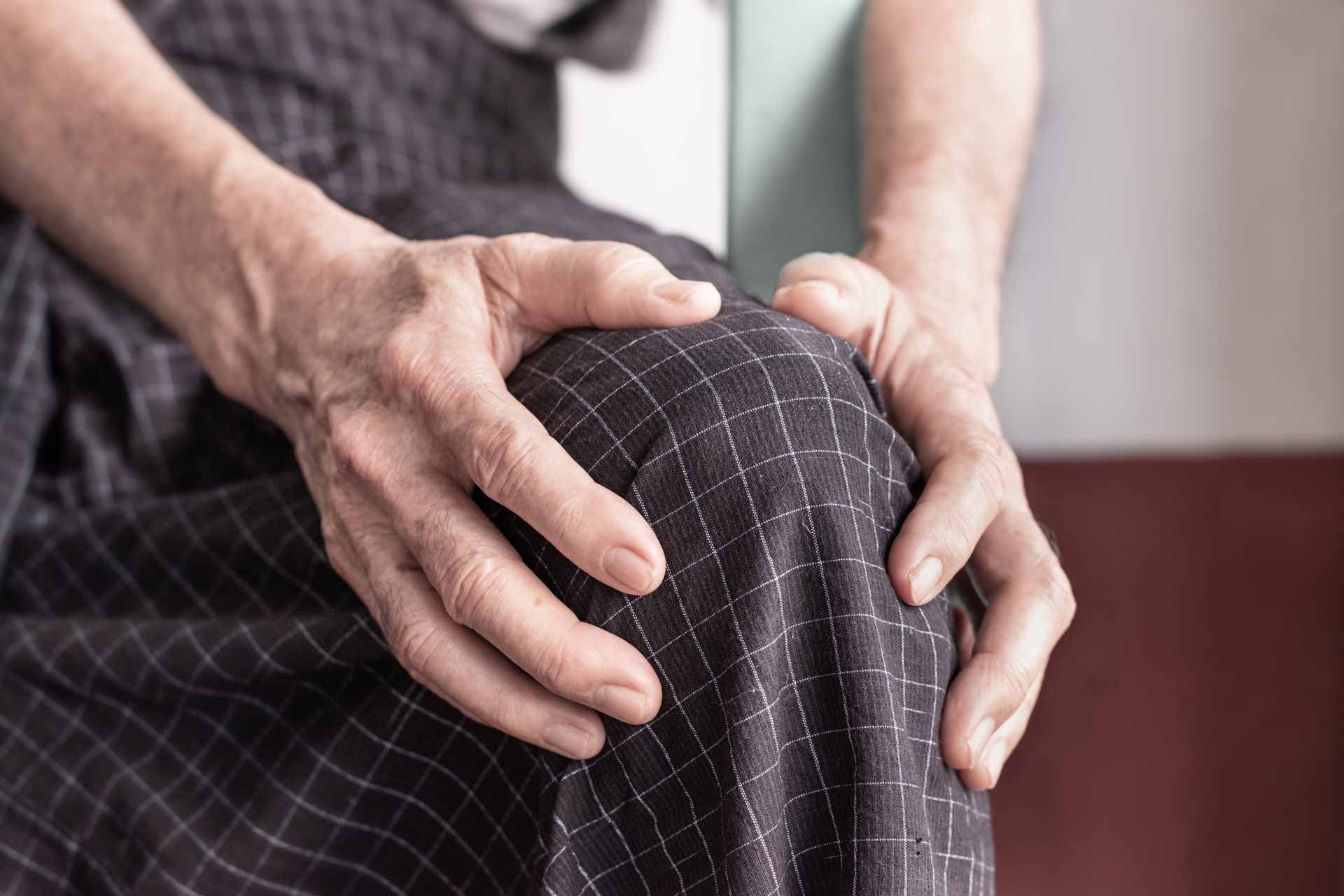 Hands holding a knee in pain, with a checkered fabric background