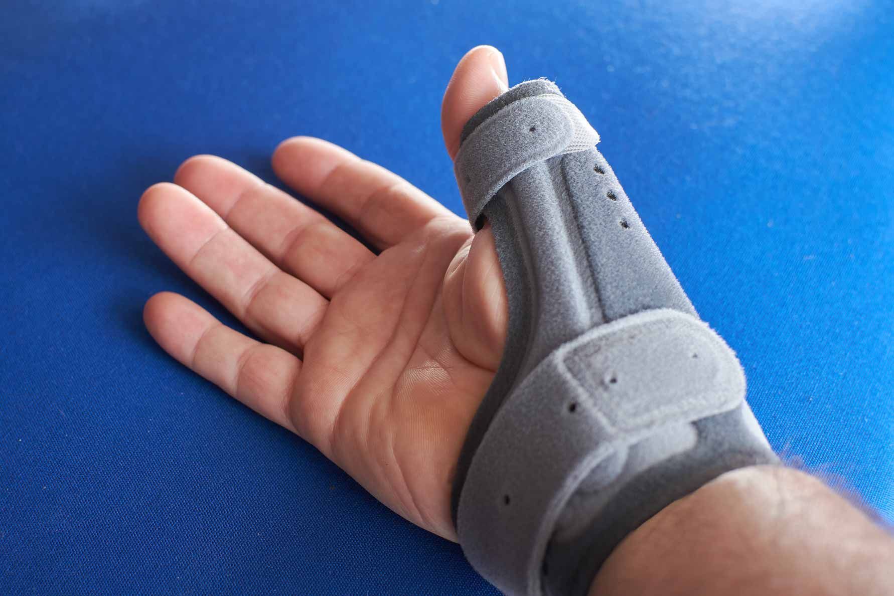 Hand wearing a gray thumb brace on a blue surface