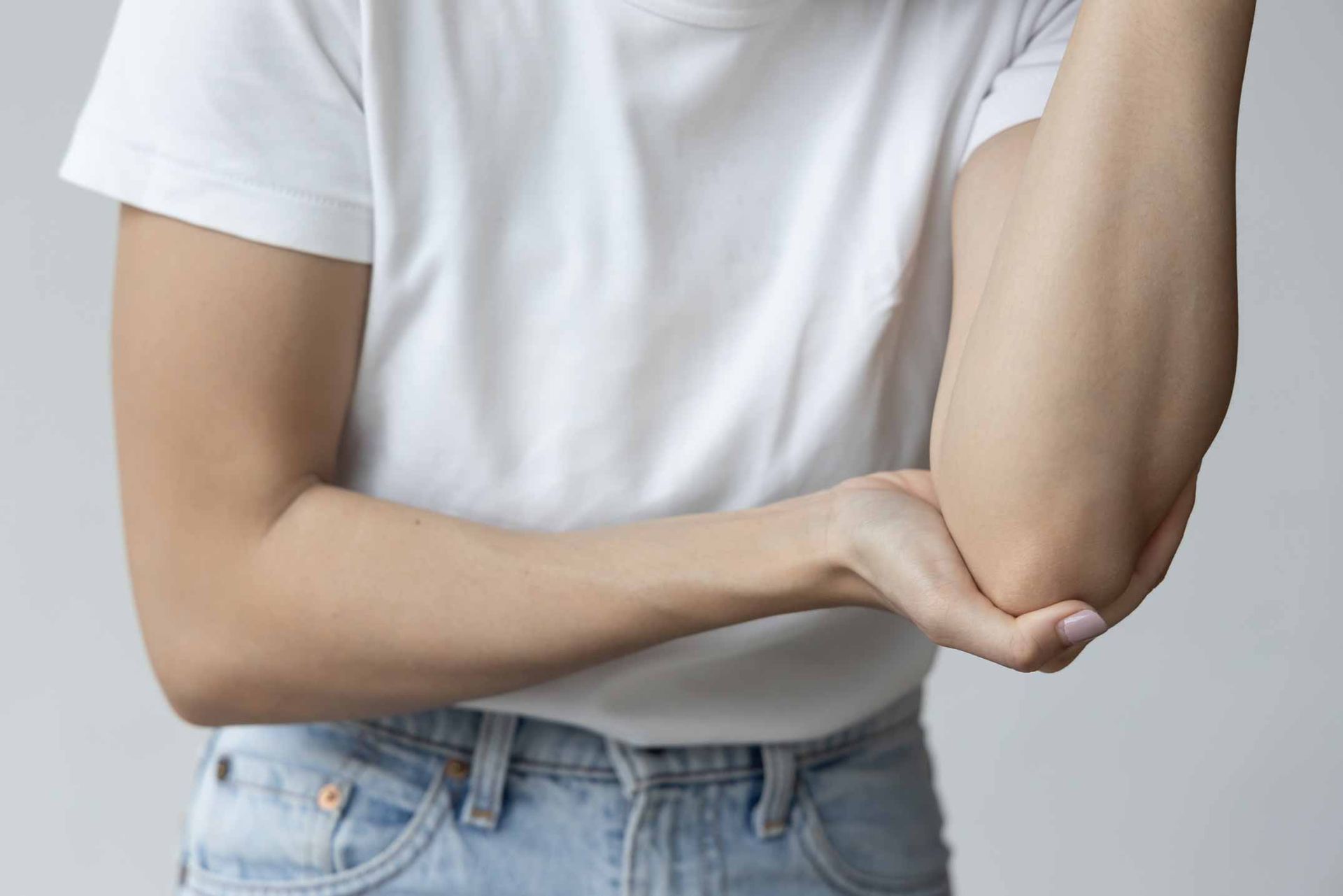 Person in white shirt holding their bent elbow, showing arm pain or injury