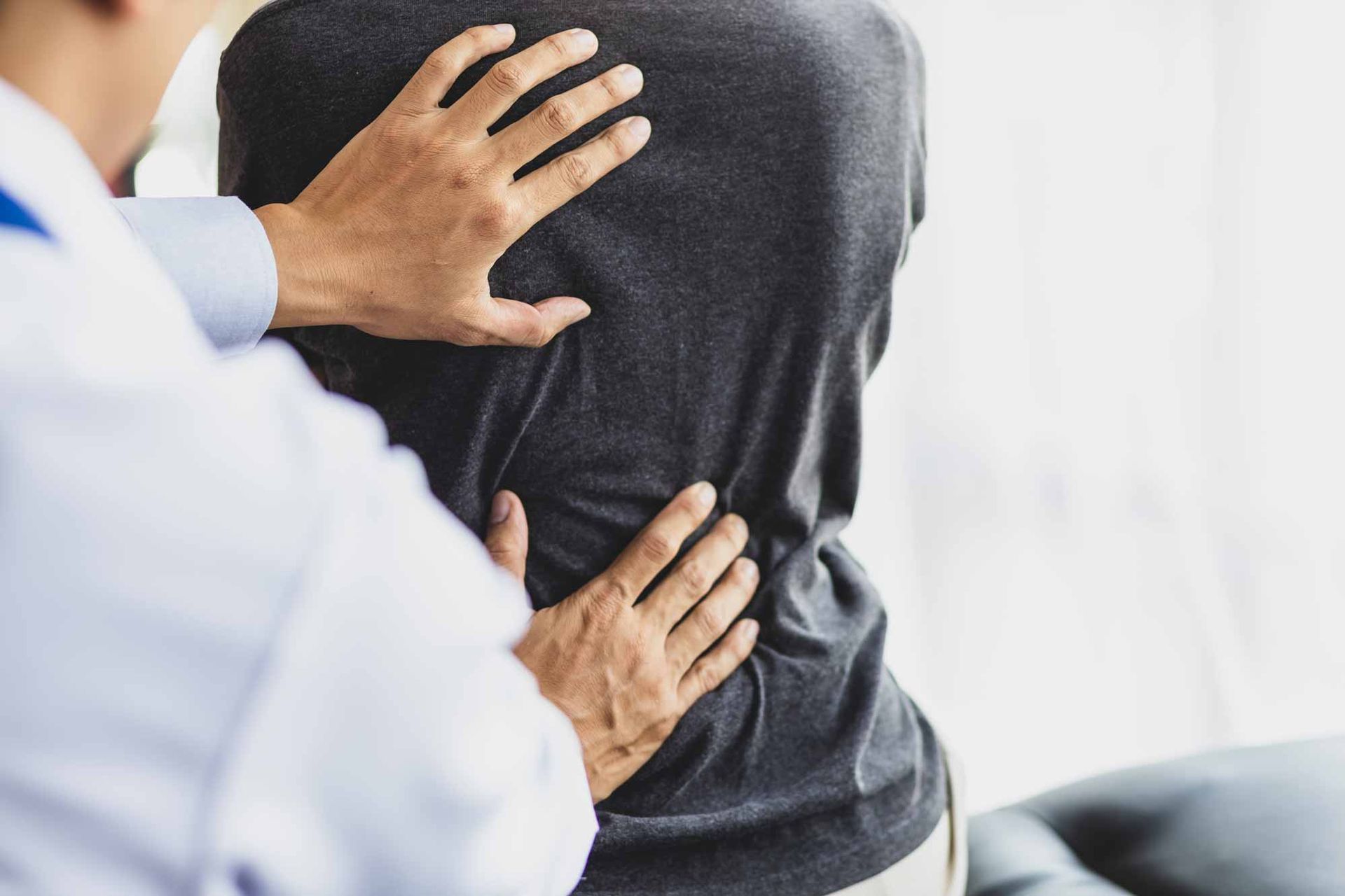 Doctor examining a patient’s back in a clinic, with hands placed on the spine.