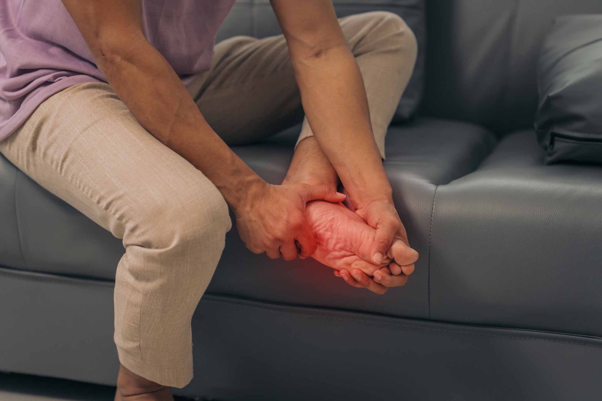 Person seated on a couch clutching a swollen, red foot in pain
