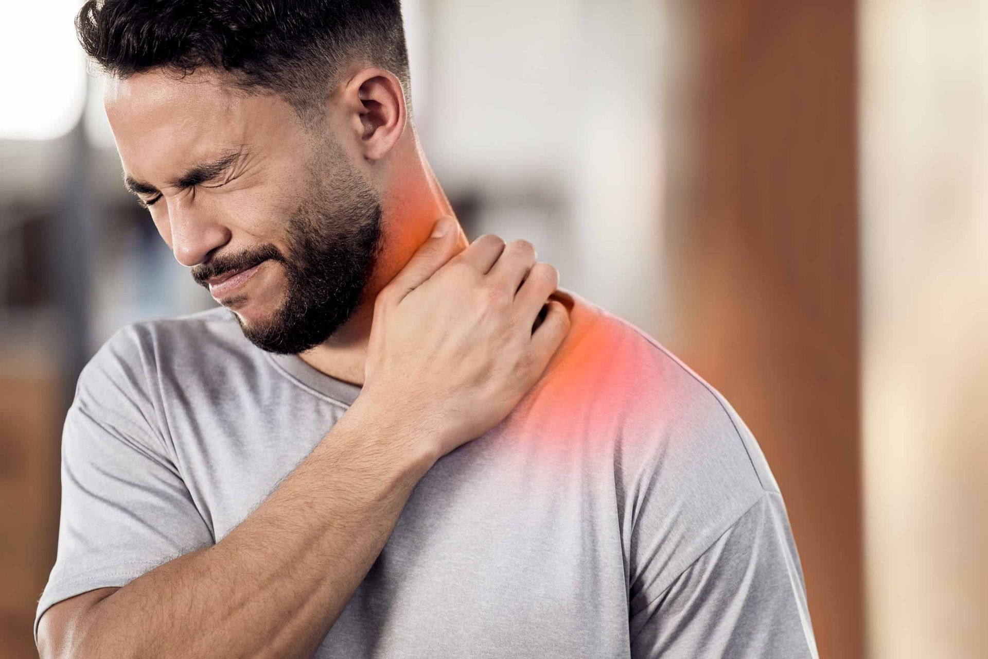 Man grimacing and holding his neck, showing pain with a red-highlighted shoulder area