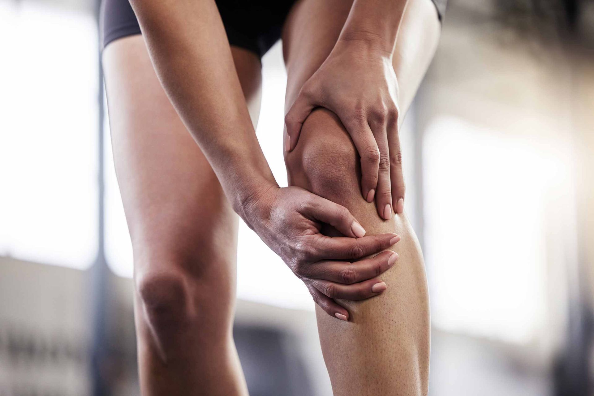 Person holding a sore knee with both hands, suggesting knee pain or injury