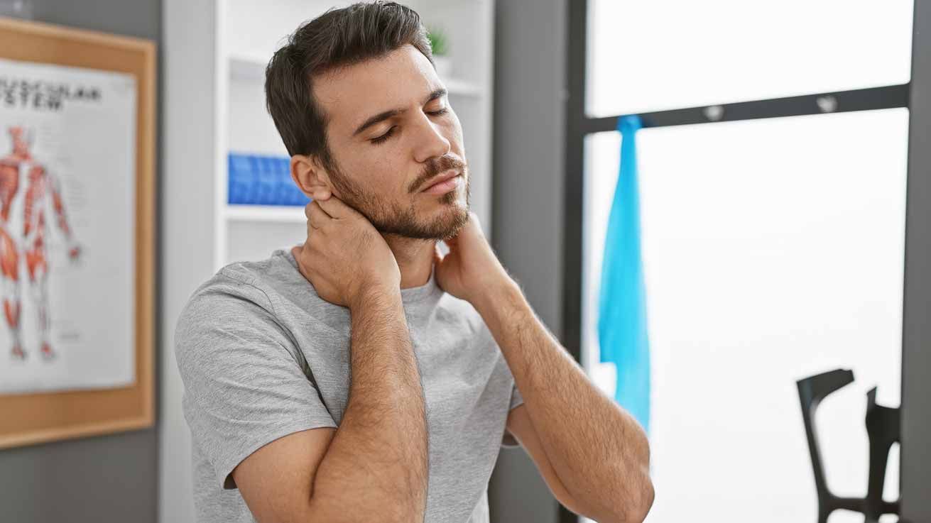 Person in a gray shirt massaging their neck, looking uncomfortable in an office setting.