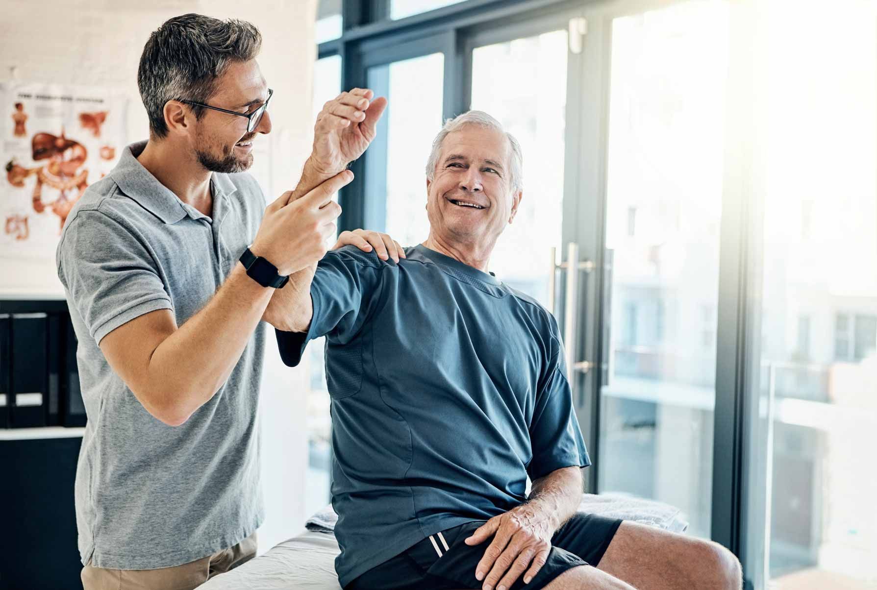 Physical therapist guiding a seated patient through arm exercises in a bright clinic room