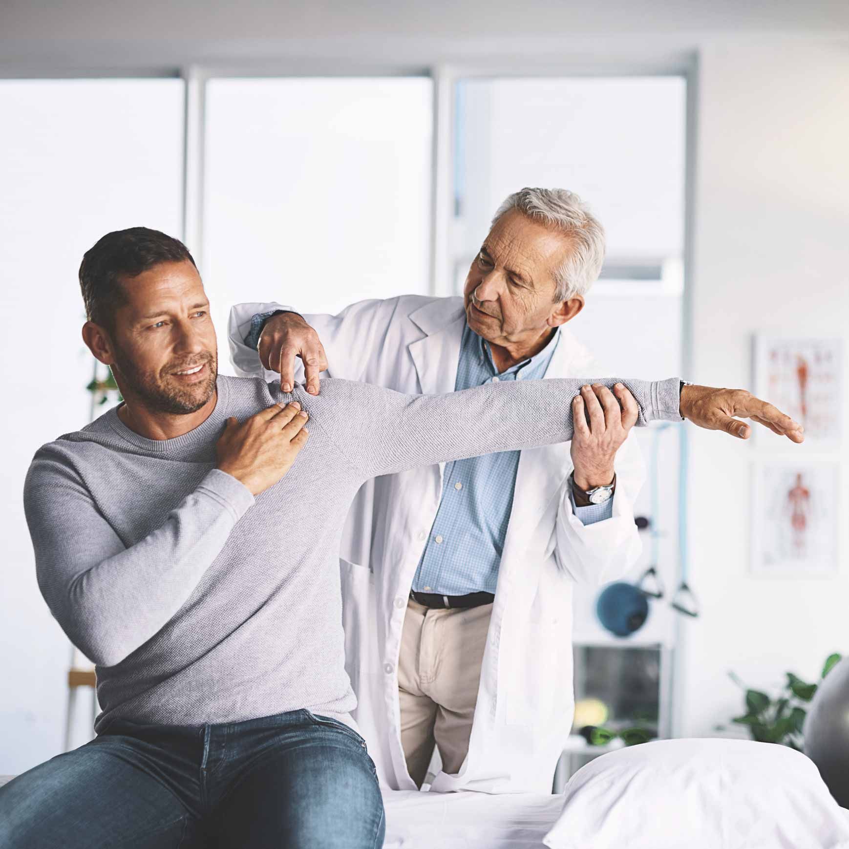 Physical therapist helping a seated patient stretch his arm in a bright clinic room