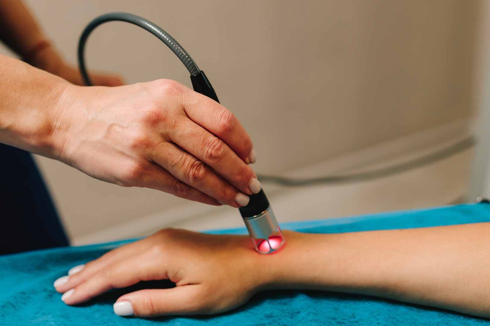 Hand using a laser device on a person's forearm during a treatment session