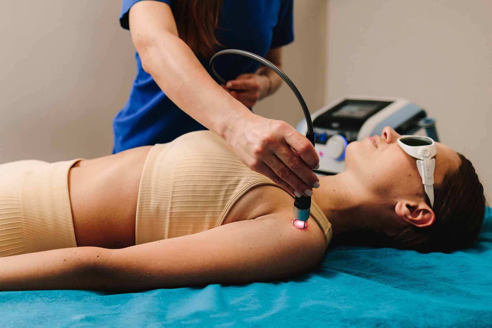 Spa treatment with practitioner using a handheld device on a woman lying on a blue treatment table