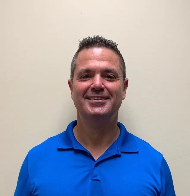 Smiling man in a bright blue polo shirt standing against a plain beige wall