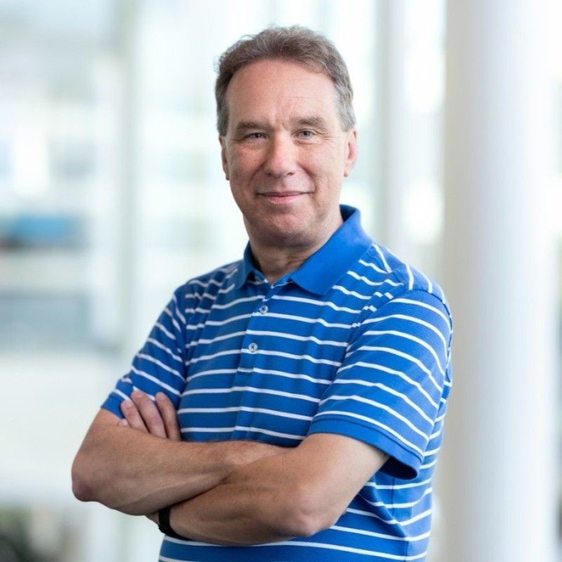 Person in a blue striped polo shirt, arms crossed, standing indoors with a blurred office background.