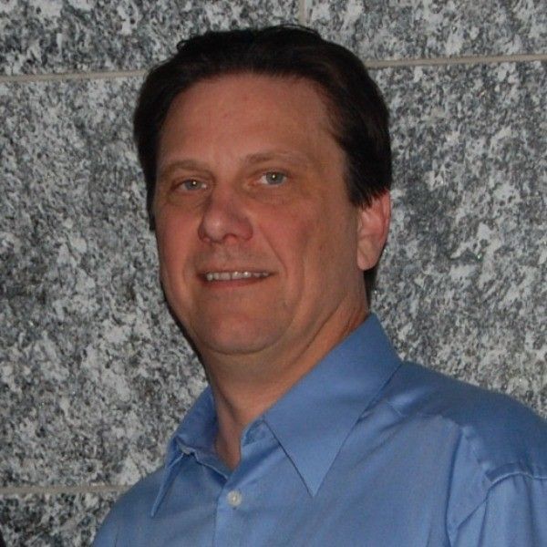 Man in a blue shirt posing against a gray stone wall