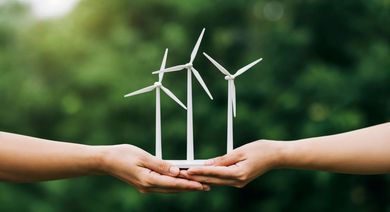 Two hands holding white wind turbines against a green blurred background