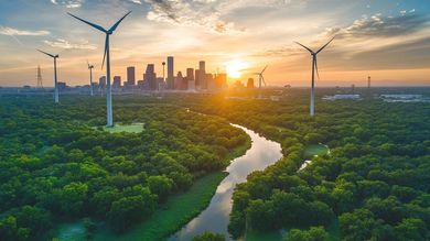 Sunset city skyline beyond lush forest with wind turbines and a winding river
