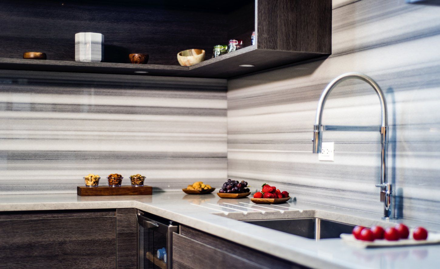 Modern kitchen with a sink, faucet, white countertops, dark wood cabinets, and fruit.