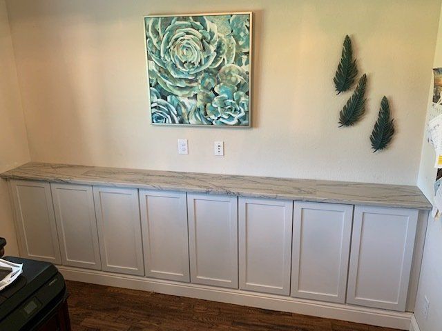 White cabinets with a gray countertop and wall art on a beige wall.