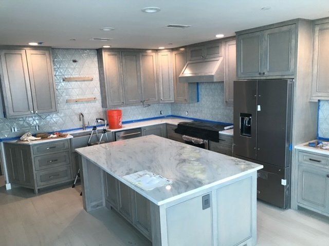 Kitchen under construction with gray cabinets, island, and stainless steel appliances.